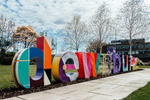 Large scale colourful 3- dimensional letters spelling 'Dewsbury', sit outside on grass